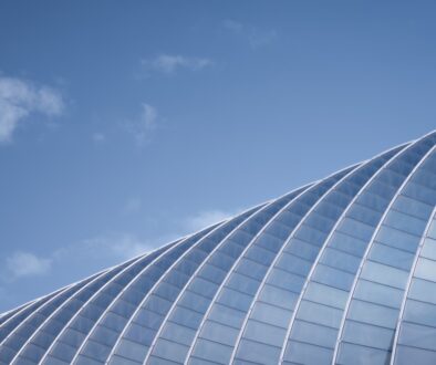 A,Modern,Glass,Structure,Arches,Gracefully,Against,A,Clear,Blue