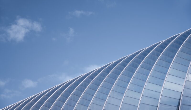 A,Modern,Glass,Structure,Arches,Gracefully,Against,A,Clear,Blue
