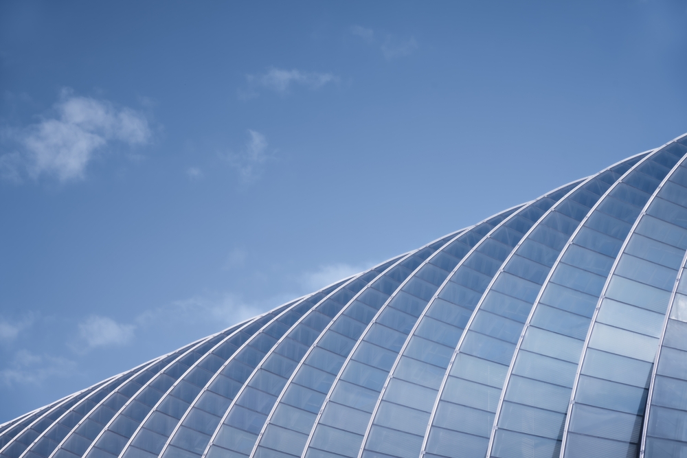 A,Modern,Glass,Structure,Arches,Gracefully,Against,A,Clear,Blue